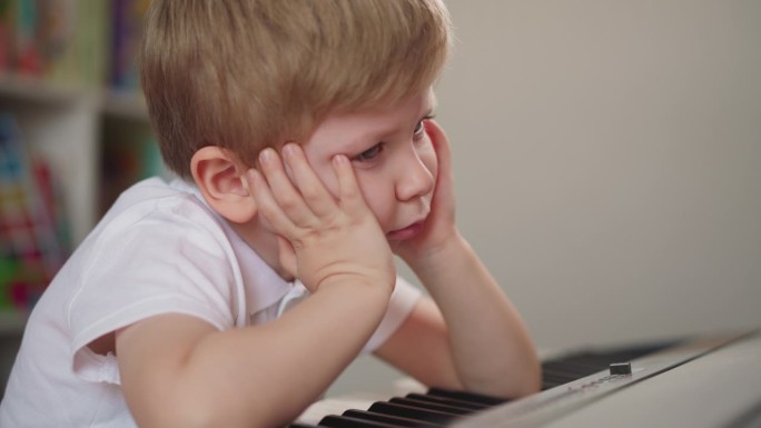 小男孩倚着双手，在钢琴前悲伤地喘着气