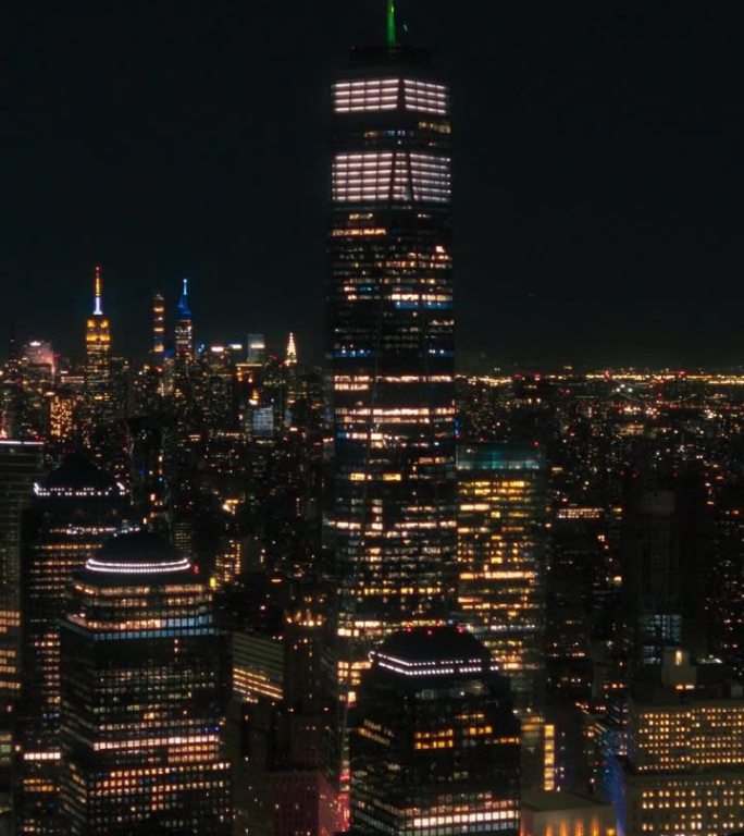 垂直屏幕:世界贸易中心一号大楼的夜间航拍画面，里面的办公室有灯光。直升机在建筑物周围拍摄弧线，俯瞰纽