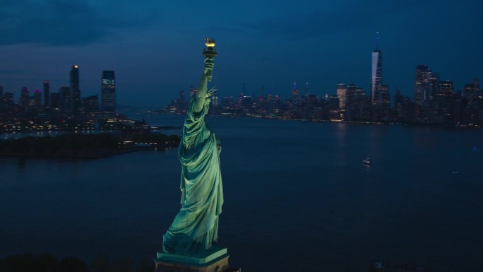 空中直升机的电影观自由女神像与曼哈顿天际线的城市景观在晚上。日落时纽约摩天大楼和泽西城建筑的全景