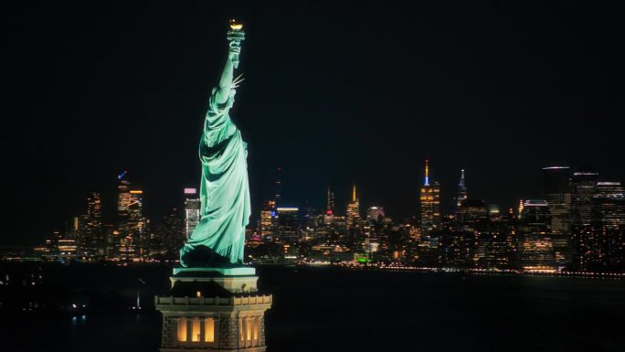 美国自由象征的全景航拍镜头。电影直升机在夜晚经过自由女神像。具有里程碑意义的纽约纪念碑与曼哈顿摩天大