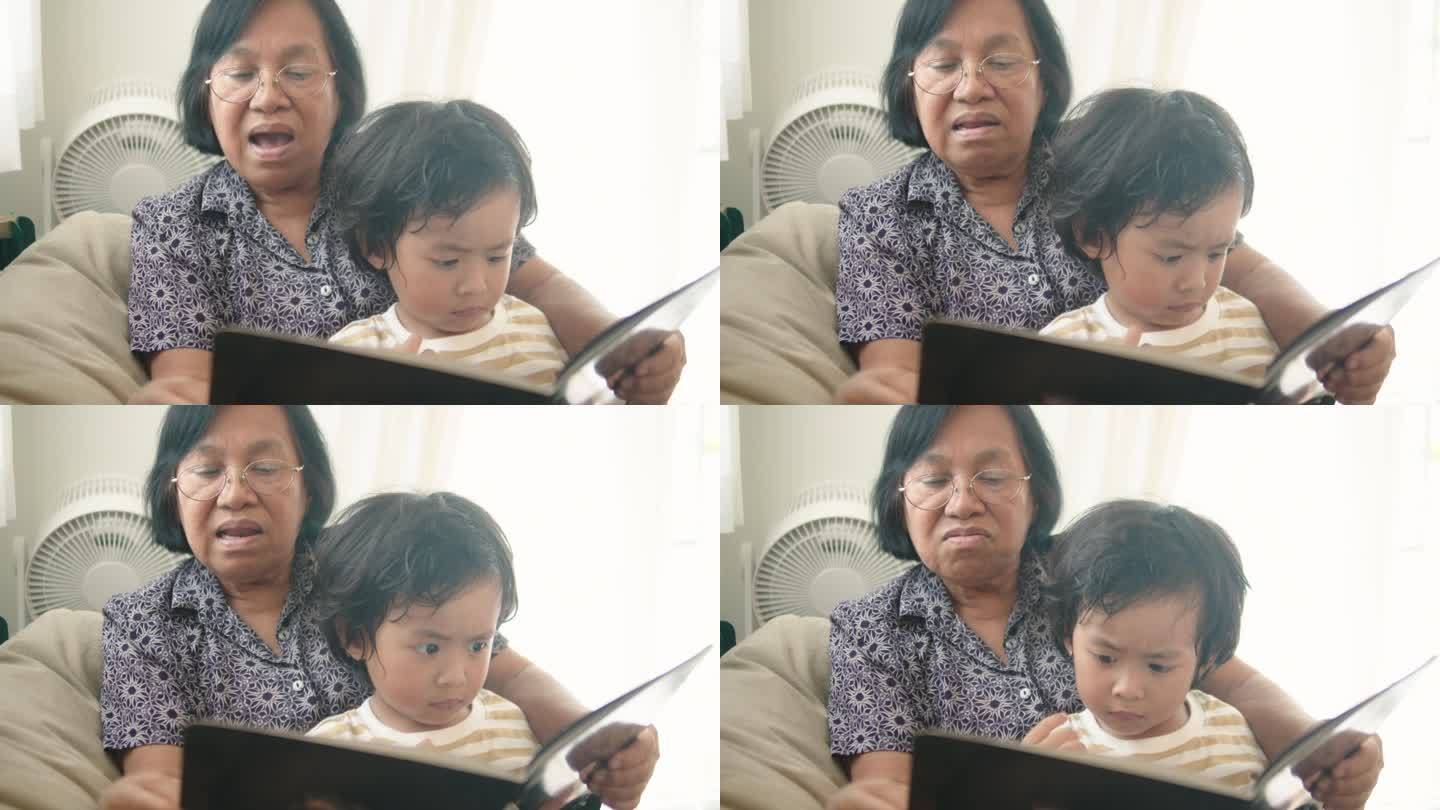 亚洲小孙子试图在家里和慈爱的奶奶一起读书。蹒跚学步的男孩喜欢和奶奶讲有趣的故事。