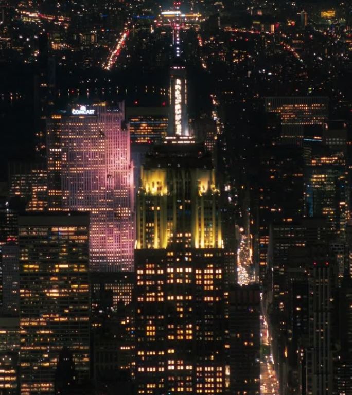 竖屏:帝国大厦塔尖和游客观景台的夜景。纽约市商业中心。曼哈顿中城建筑奇观的直升机镜头