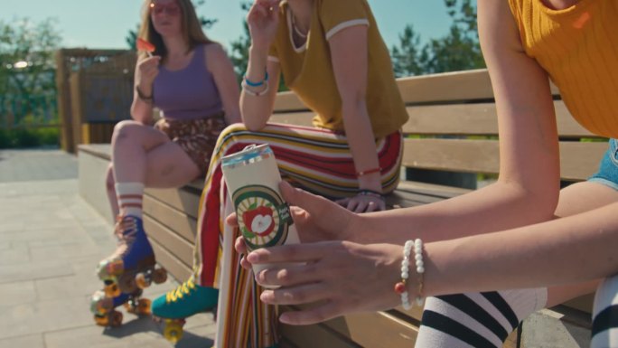 年轻的千禧一代女孩坐在长凳上，手里拿着一罐苏打水