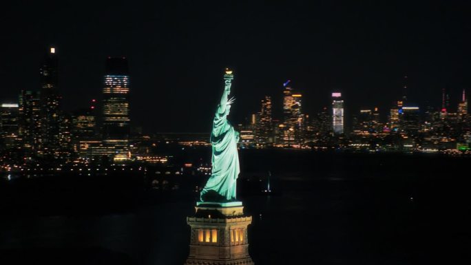 地标纽约市纪念碑与曼哈顿摩天大楼的背景。夜间自由女神像的全景航拍镜头。直升机观光，风光无限