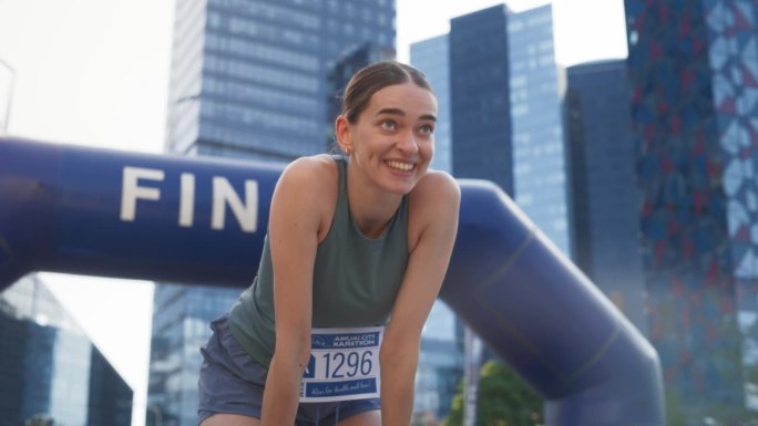 一位快乐的城市马拉松女选手穿过终点线，庆祝她的胜利。女冠军实现目标并享受她的成就