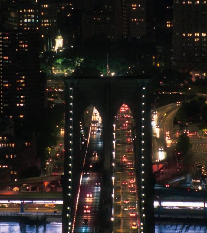 垂直屏幕:夜间从直升机上俯瞰的纽约市天际线。著名的摩天大楼和布鲁克林大桥上的美国国旗。繁忙多样的大都