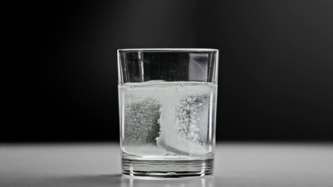泡腾片落入玻璃杯中的淡水(特写)。在演播室拍摄的宏观上制作运动生活方式的健康饮料。服用药丸和悬浮液缓