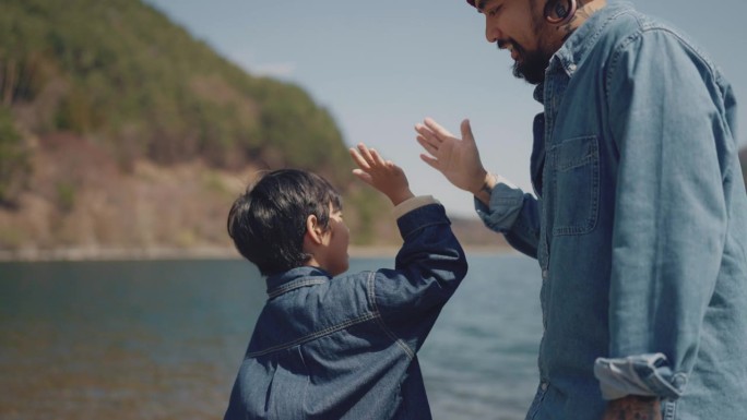 骄傲英俊的父亲教他的小儿子向湖里扔石头，父子俩击掌庆祝成功。