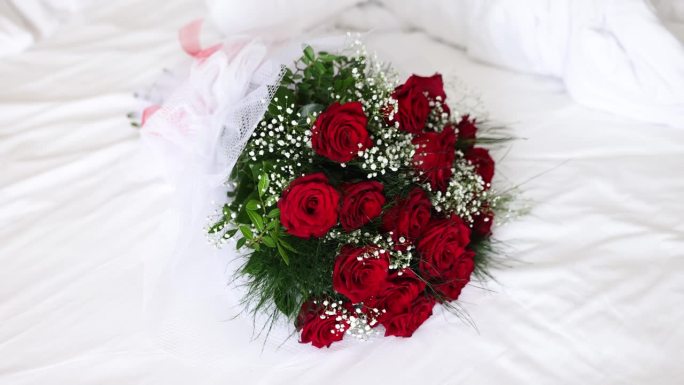 婚礼的红玫瑰花束放在床上，上面铺着白毯子