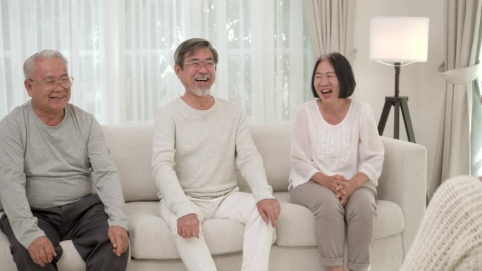 一群快乐的亚洲老人坐在沙发上谈论有趣的故事。