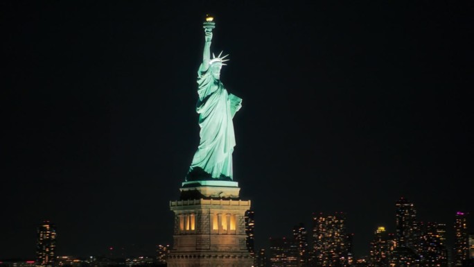 空中直升机观影自由女神像与曼哈顿天际线的城市景观与灯光在办公大楼和摩天大楼在晚上。纽约天际线全景
