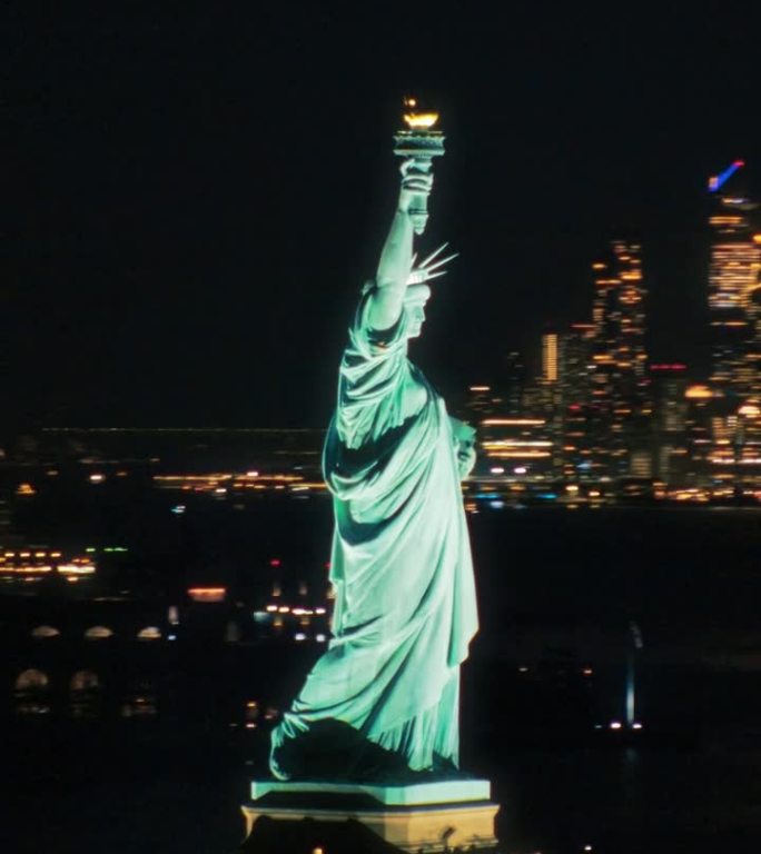 垂直屏幕:空中直升机电影的自由女神像与曼哈顿天际线城市景观与灯光在办公大楼在晚上。纽约天际线全景
