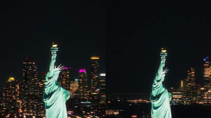 垂直屏幕:空中直升机电影的自由女神像与曼哈顿天际线城市景观与灯光在办公大楼在晚上。纽约天际线全景