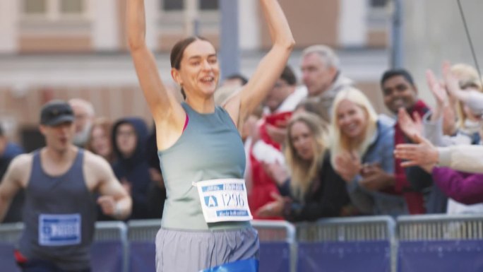 马拉松女运动员在观众的欢呼声中冲过终点线的慢镜头。快乐的成功女性庆祝胜利，为自己的成就感到鼓舞
