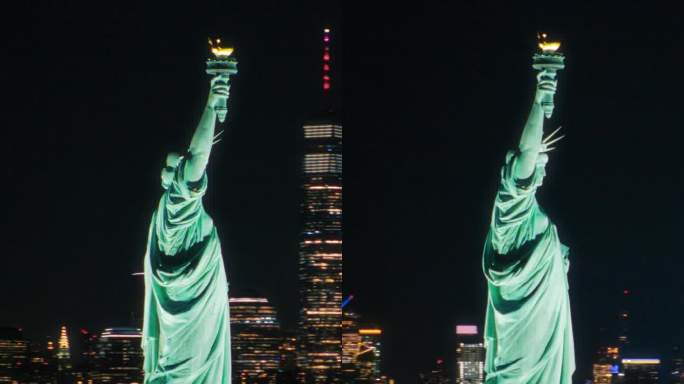 垂直屏幕:美国自由象征的全景航拍镜头。电影直升机在夜晚经过自由女神像。地标性的纽约纪念碑和曼哈顿摩天