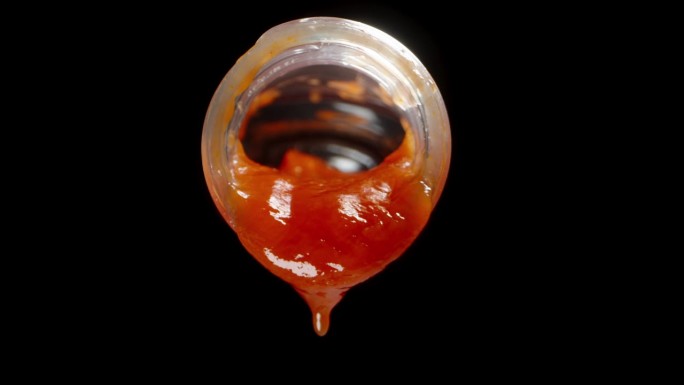 番茄酱从瓶子里滴出来，特写。孤立在一个黑色的背景。