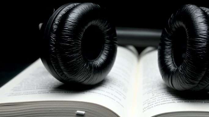 书和黑色耳机在黑色背景。有声书概念。