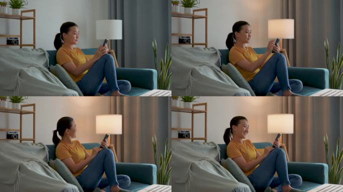 亚洲女人坐在客厅的沙发上用智能手机开灯。