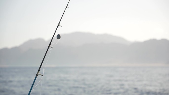 鱼线上的钓竿和钓鱼沉片的特写，准备在海里钓大鱼。日落时背景中的山脉