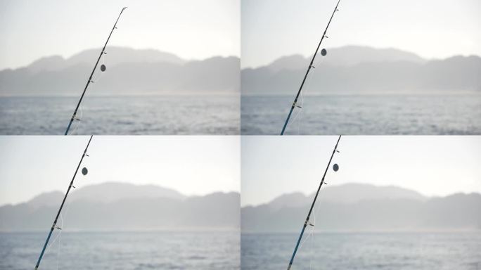 鱼线上的钓竿和钓鱼沉片的特写，准备在海里钓大鱼。日落时背景中的山脉