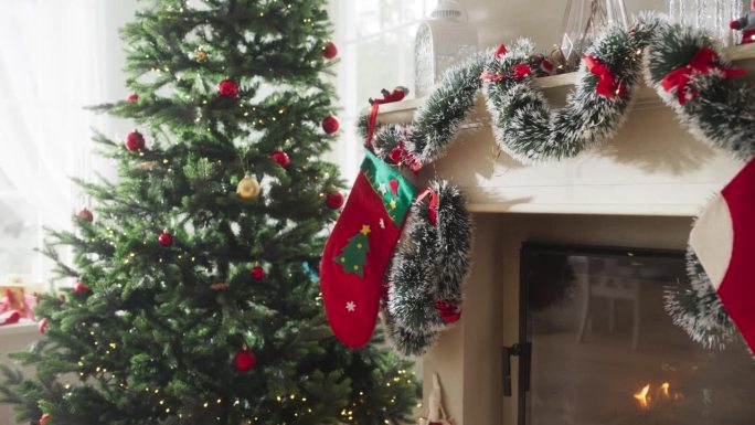 在一个和平的下雪的圣诞节早晨描绘假期的魔力:近距离观察圣诞树旁边装饰着袜子的壁炉。绿色和红色的花环，