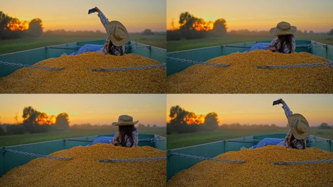 快乐的女农学家躺在玉米粒堆上，在日落时分用智能手机在拖车里自拍