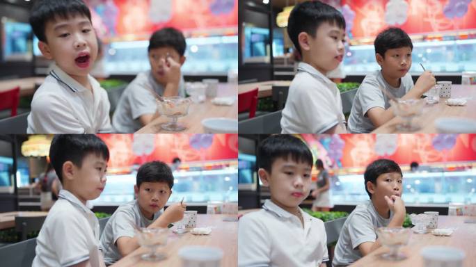 两个年轻的亚洲男孩在一家舒适的咖啡馆里一边吃着冰淇淋一边愉快地交谈。两个男孩都带着灿烂的笑容品尝着他