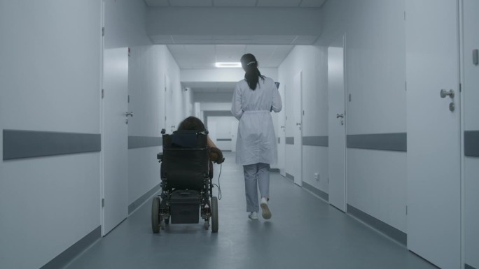 女医生在诊所走廊与坐轮椅的妇女交谈
