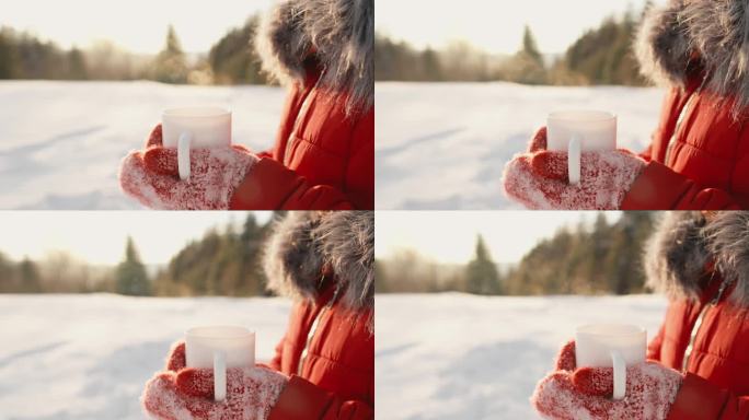 冬天的院子里，一个女人拿着一个白色的杯子，里面装着热气腾腾的热饮。美味的茶或芳香的咖啡。雪里的热葡萄