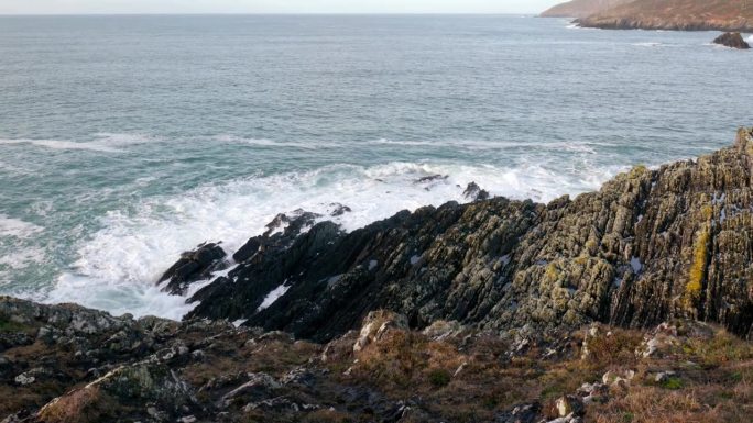 岩石嶙峋的海岸线，锯齿状的岩石在海浪的冲击下屹立不倒。深蓝色的大海，白色的泡沫从波浪。缩小