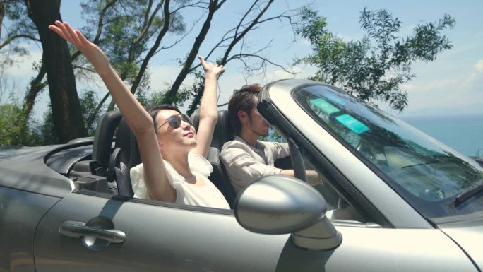 年轻的亚洲夫妇有乐趣驾驶和骑在海边的公路上敞篷车?