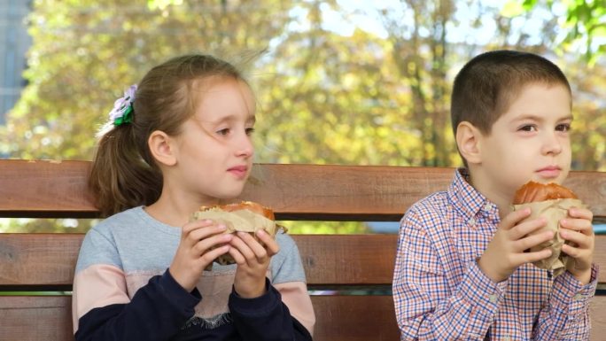 夏天，一个男孩和一个女孩坐在城市的长凳上吃汉堡，街边小吃。