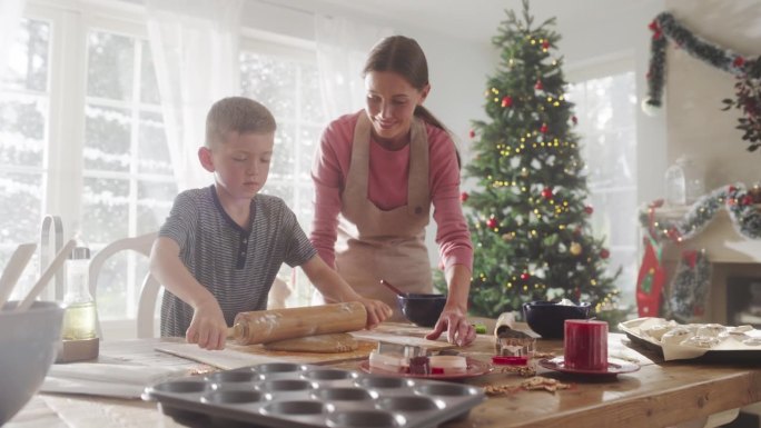 慢动作肖像的母亲和儿子准备烤姜饼在圣诞节。可爱的小男孩帮妈妈做家务和做饭，一起度过假期