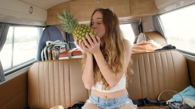 十几岁的女孩拿着菠萝，在节日期间在露营车里微笑着拍照