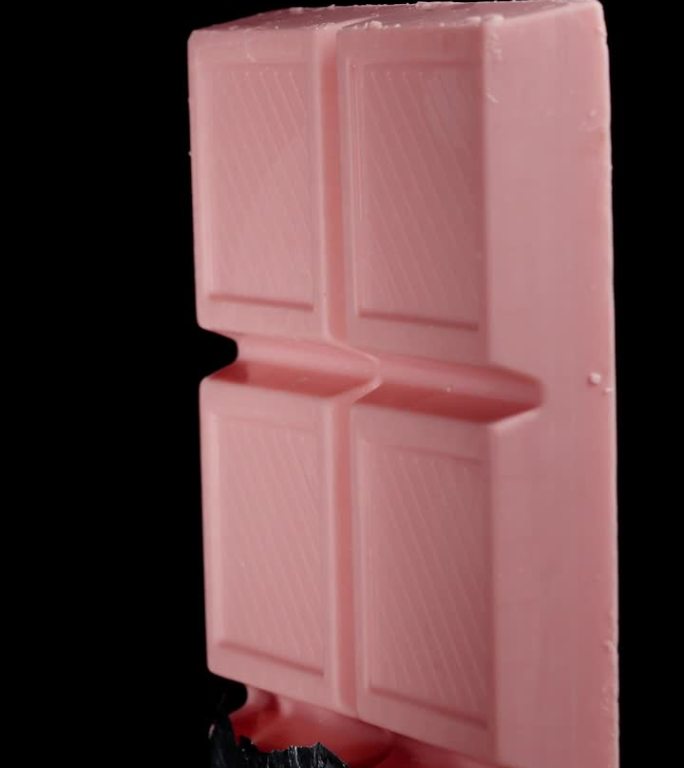 一块半包着的粉红色巧克力，用闪亮的锡箔纸包裹着，在黑色的背景上旋转，孤立的。垂直视频。