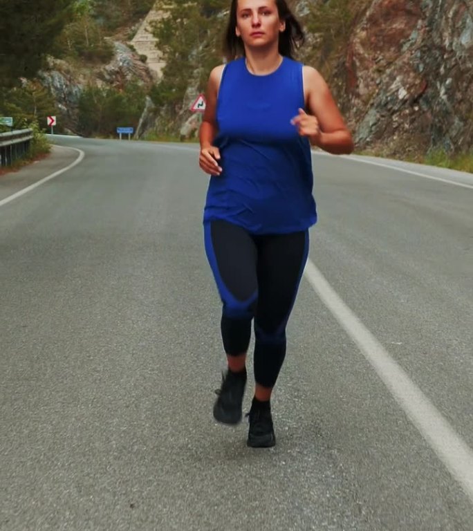 穿着运动服的女人在空旷的山路上奔跑。垂直视频