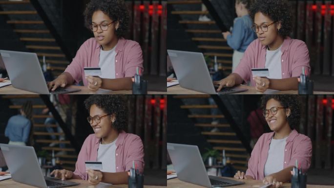 快乐的非裔美国女企业家拿着信用卡和笔记本电脑微笑地坐在办公室的办公桌前