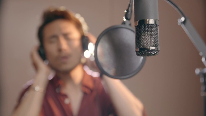 年轻的亚洲歌手唱歌录音工作室与耳机和麦克风.