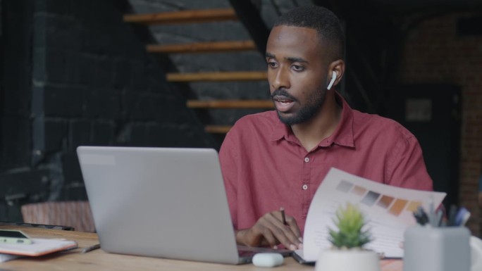 非裔美国商人用笔记本电脑和耳机进行在线视频通话，讨论在联合办公中心的工作