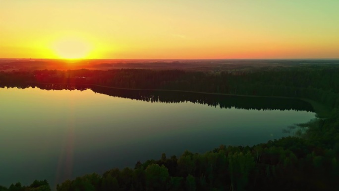 航拍无人机从右到左拍摄的风景如画的湖面平滑的日落在森林景观在晚上的时间。