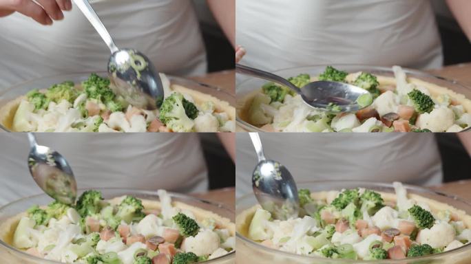 这个女人用勺子把五颜六色的卷心菜、韭菜和三文鱼片做成的馅料均匀地涂在派皮上。
