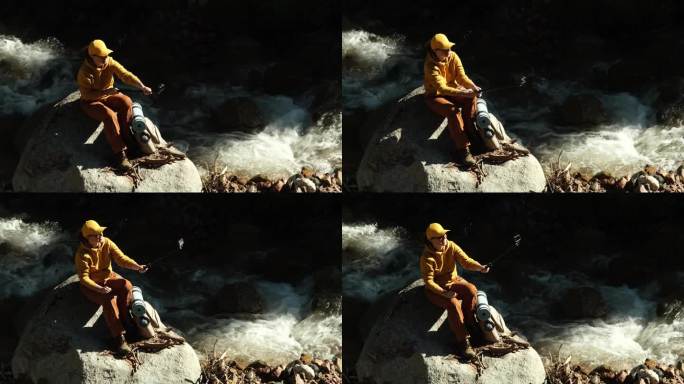 女游客坐在山涧边的石头上，用她的运动相机拍视频