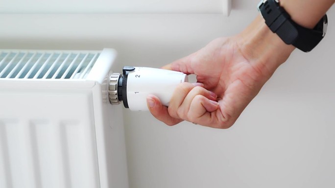 一个女人的手在转动电池加热旋钮。在家里的公寓里供暖。供热价格。