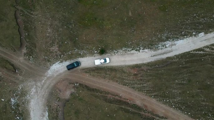 一辆黑色的SUV和一辆白色的皮卡在山间穿过田野，走在人迹罕至的路上