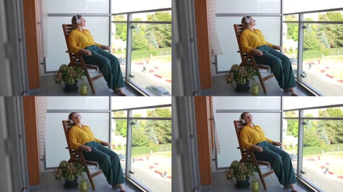 一个安静的白人女人，坐在椅子上听音乐，闭上眼睛，在家里享受没有压力的周末时间，拿着电话。高质量的全高