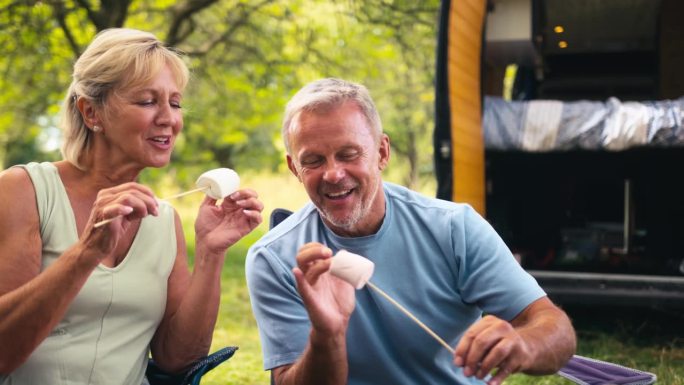 一对老年夫妇在乡下露营，开着房车在户外烤火，吃棉花糖