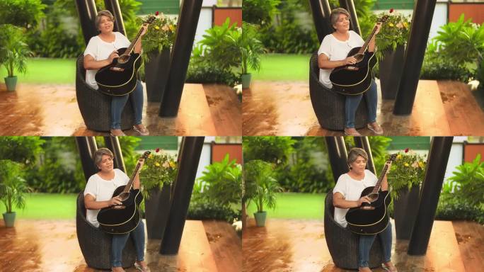快乐的成熟中年妇女坐在椅子上唱歌，弹吉他，享受音乐，在户外度过闲暇时光。美丽微笑的印度女吉他手练习乐