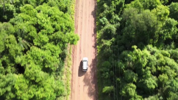 无人机自顶向下的视角跟踪越野车穿越热带丛林，沿途有电线