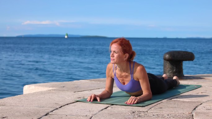在一个阳光明媚的日子里，中年妇女躺在海边的瑜伽垫上，靠在胳膊肘上