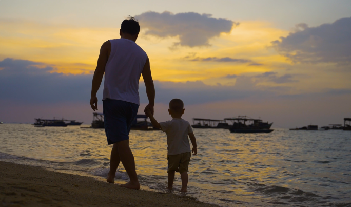 父子海边散步温馨爸爸牵着儿子海边日落夕阳